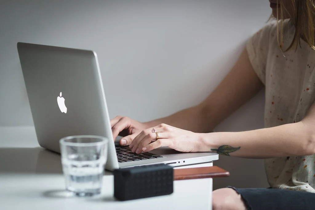 Zdjęcie przedstawia osobę, która rozpoczyna używanie systemu rezerwacji online. Widoczny laptop, biurko oraz ręce kobiety.