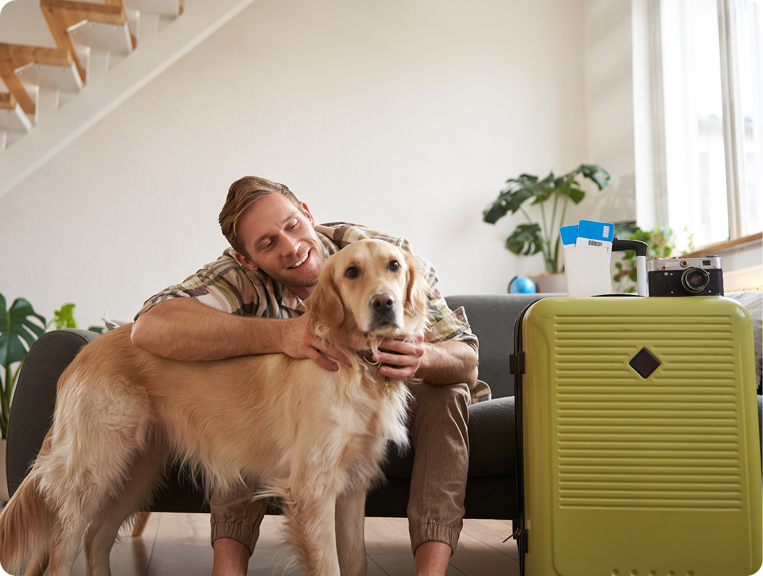 Zadowolony właściciel przytula psa obok zielonej walizki - system rezerwacji dla hoteli dla zwierząt.