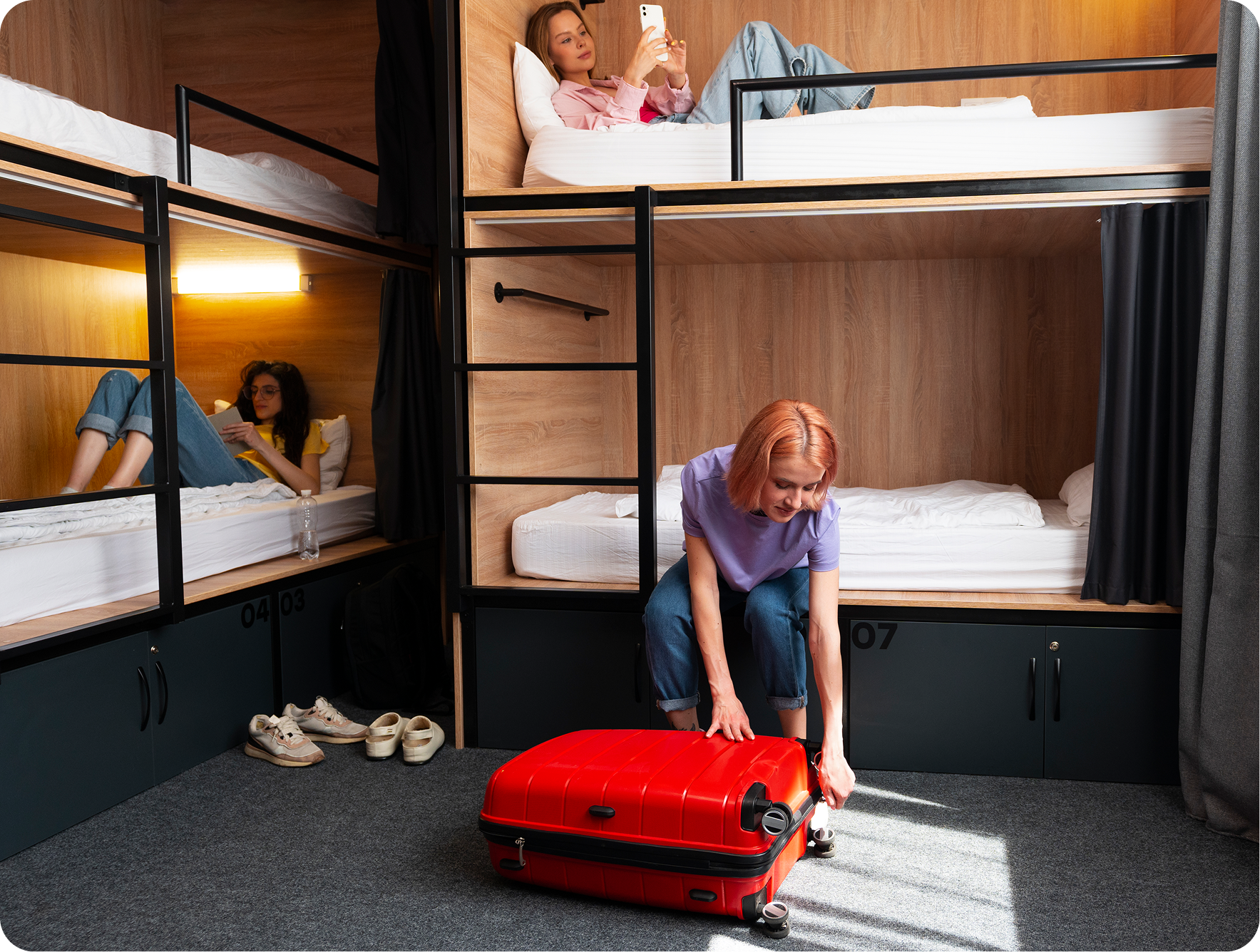 Interior moderno de un hostal con literas de madera y una maleta de viaje roja.