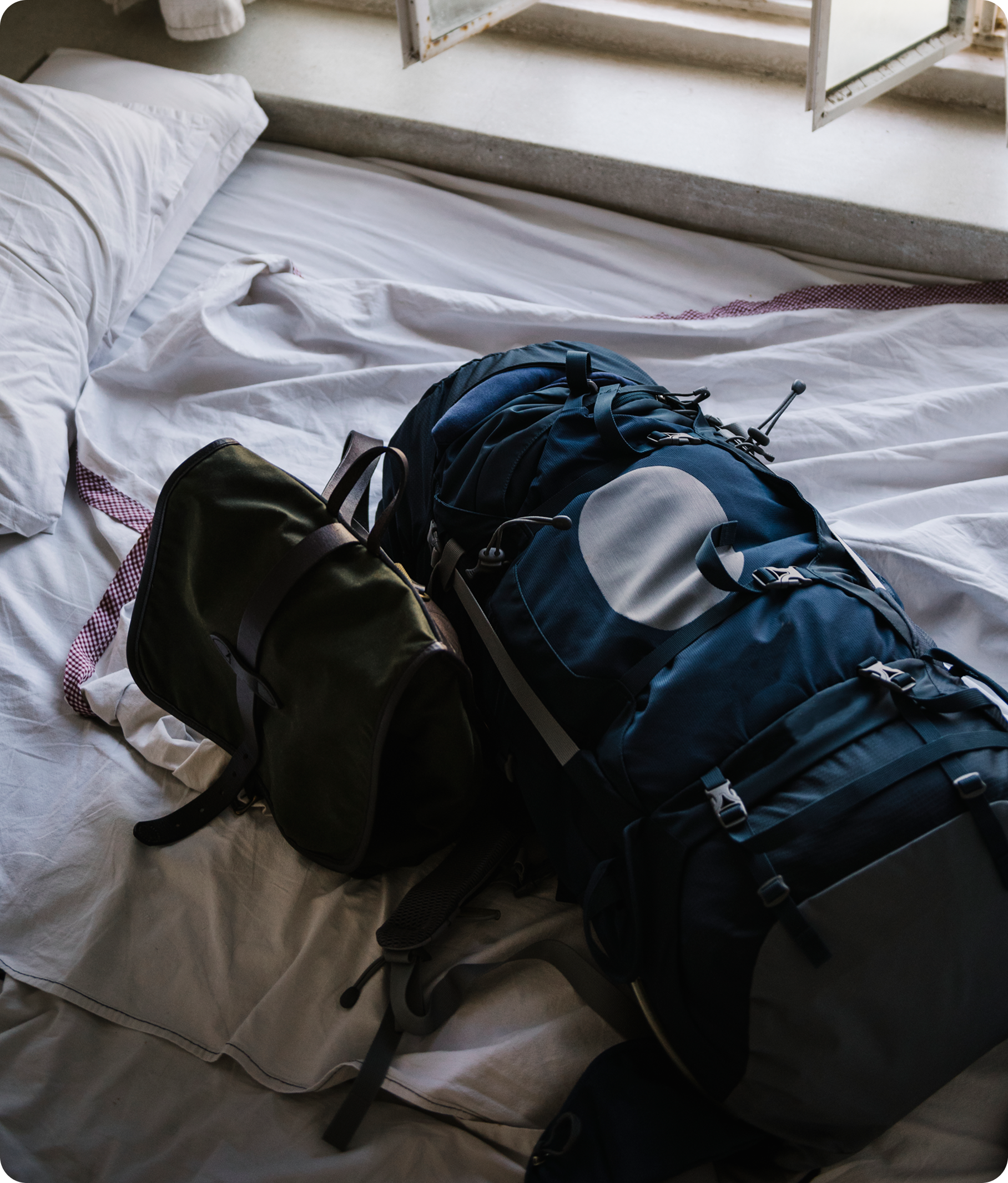 Mochilas de turistas dejadas sobre una cama en un hostal asequible y cómodo.